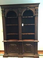 Front view of the full wall unit bookcase showing the dark wood finish, two upper large arched shelf sections, and two lower paneled cabinet doors.