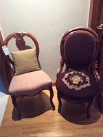 Two occasional chairs side by side, one with dark purple embroidered upholstery and armrests, the other with light beige upholstery and a carved open backrest.