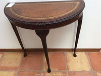 Front view of the half moon table showcasing the carved clawfoot legs and scalloped wooden apron.
