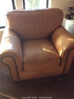 Front view of oversized leather club chair showing cushioned back, seat, and arms with nailhead trim on arm edges.