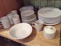Photo showing multiple plates, mugs, creamer, and sugar bowl arranged on countertop to display basketweave pattern and item variety.