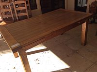 Photo of the overall dining table showing rectangular solid wood design with four legs and plank-style top surface.
