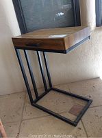 Side view of the side table showing the wood top with drawer and black metal frame base allowing placement over a sofa seat.