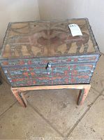 Wooden travelling chest with carved and painted elephant motifs and metal latch, displayed on wooden stand, showing overall item.