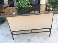 Side view of the outdoor bar showing beige fabric panel under the glass top and black wrought iron frame.