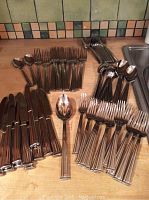 Full view of entire cutlery set including knives, forks, spoons, and serving pieces laid out on a wooden surface.