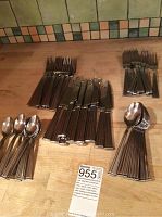 Full cutlery assortment on a wooden countertop including forks, spoons, knives, and serving pieces.