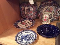 Photo of six serving pieces including a floral pitcher and various decorative plates with floral and patterned designs on a wooden surface.