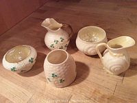 Five-item set of Belleek Irish porcelain on wooden surface showing shamrock decorations and overall condition.