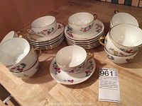 Thirteen sets of Limoges tea cups and saucers stacked in groups on a table, showing floral designs and gold trim on the cups and saucers.