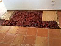 Full view of vintage camel blanket showing frayed and worn beige areas on the right side and patterned areas on the left, laid on a tile floor.
