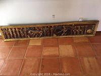 Full view of the wooden frieze panel resting on tiled floor against wall, showing entire length and carved details.