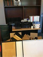 Overview of office items including binders, trays, boxes, Epson printer on table, storage shelves with binders and papers, whiteboards in foreground.