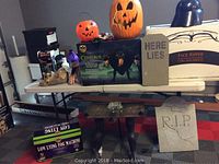 Wide shot showing the entire Halloween decor lot including Cerberus animatronic box, fog machine box, tombstones, pumpkin buckets, and flying monster figure.