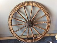 Front view of a large wooden and stone wagon wheel with detailed turned spokes and a stone hub, showing craftsmanship and size relative to tile flooring.