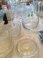 Photo of assorted clear glassware including cut glass glasses, clear glass bowls and plates, stemmed wine glasses, and a small clear glass pitcher placed on a table.