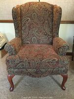 Front view of wing back chair showing paisley upholstery and Queen Anne legs.