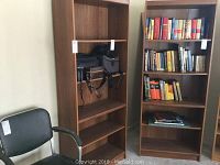 Photo of two laminate bookcases side by side, one containing camera bags, the other filled with books.