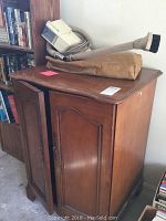 Full view of the wooden two-door cabinet with a smooth finish, showing signs of wear, and the vacuum placed on top.