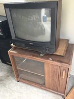 Front and slightly angled side view of the black RCA CRT television sitting on top of a wooden cabinet with glass doors, showing the TV screen and manual buttons.