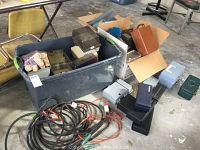Overview photo showing the lot contents including large plastic bin holding smaller boxes, extension cords and battery cables coiled on ground, various boxes and tackle box.