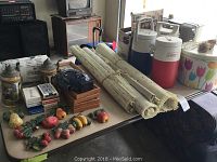 Photo of multiple items including the drink coolers (Coleman and Igloo), metal canister, rolled vinyl blinds, beer steins, decks of cards, and the table fan on a white table.