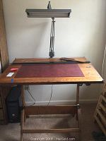 Front view of the drafting table with the attached adjustable lamp and maroon mat on the tabletop.
