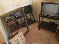 Photo showing gold framed mirror with ornate detailing, frameless mirror, two framed floral prints, and corner of the TV stand and TV.