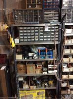 Metal shelving unit containing various boxes and organizers filled with nuts, bolts, screws, computer fans, and other parts.