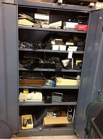 Full view of the metal shelving cabinet with various electronic and communication items.