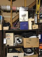 Five shelves filled with assorted wires, cables, boxes, fan in box, rolls of tape and rubber hoses in basement.