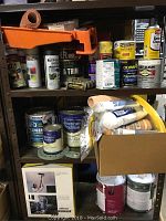 Five shelves filled with assorted paint cans, spray paints, and painting accessories such as rollers and brushes. Various brands including Rust-Oleum, Zinsser, American Tradition, and Olympic visible.