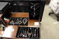 Overview of multiple brass and crystal component necklaces arranged on black pads and wooden tables