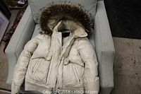 White Mackage jacket with raccoon fur hood shown on a chair, displaying overall condition and style.