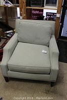 Front view of a light grey upholstered armchair with cushion seat and back. Visible wear and stain.