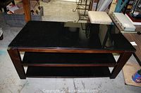 TV stand front view with black glass top, two lower shelves, and dark wood frame