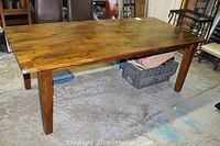 Full view of solid wood rectangular dining table with visible wood grain and warm brown finish. The table has sturdy square legs and shows general usage wear.