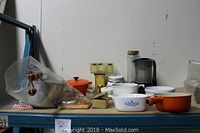 Overall view of the lot items on shelf including cast iron pot, CorningWare dishes, bowls, and small kitchen accessories