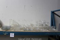 Long shelf showing all glassware items including plates, wine glasses, a pitcher, and bowls lined up for viewing.