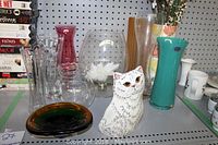Shelf display of various glass vases, bowls, and a cat figurine arranged on a pegboard background.