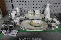 Overview of porcelain items on shelf including serving platters, mugs, small jars, egg holders, and vases with floral decorative motifs.
