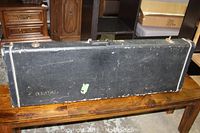 Exterior full view of black rectangular guitar case, showing scuffed and worn areas on the surface.