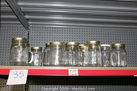 Shelf displaying 10 clear glass jars varying in size with metal and plastic lids