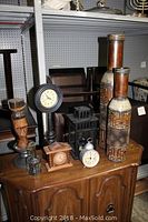 Wooden decorative bottles, black metal lantern, two clocks, carved wooden figure, and wooden coasters on wooden cabinet