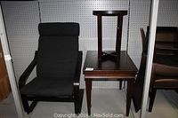 Fabric armchair with wooden frame and side tables featuring dark wood finish, displayed against pegboard wall.