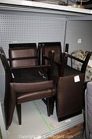 Six brown leather chairs stacked in a shelving unit, all showing surface wear and scratches on the seat upholstery.