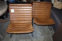 Two leather lounge chairs side by side on concrete floor.