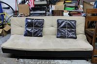 Front view of beige suede leather couch with two black leather throw pillows placed on the seat.
