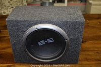 Front view of grey carpeted subwoofer box with black speaker cone and silver trim ring.