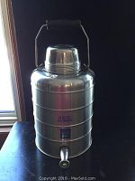 Front view of vintage aluminium cold drink server showing wooden handle, screw-on lid, spigot, and printed label on body.